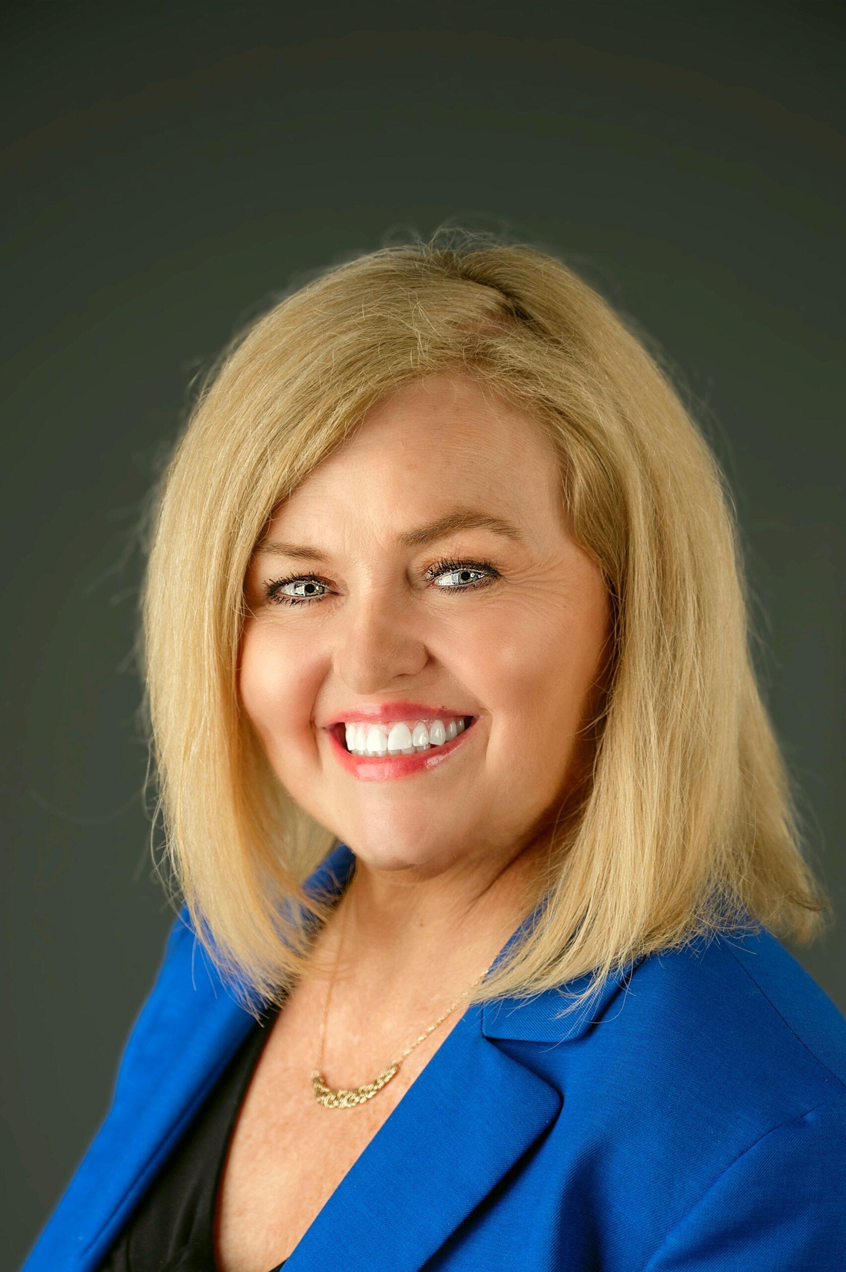 Teresa Kash Davis portrait smiling towards the camera and behind is a wooden background.