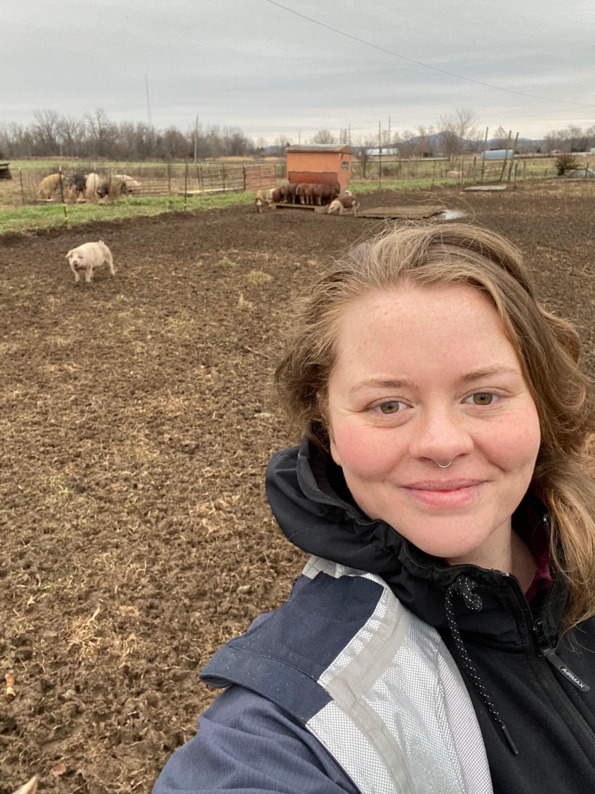 Student, Liz, taking a selfie at the College farm with pigs in the background.