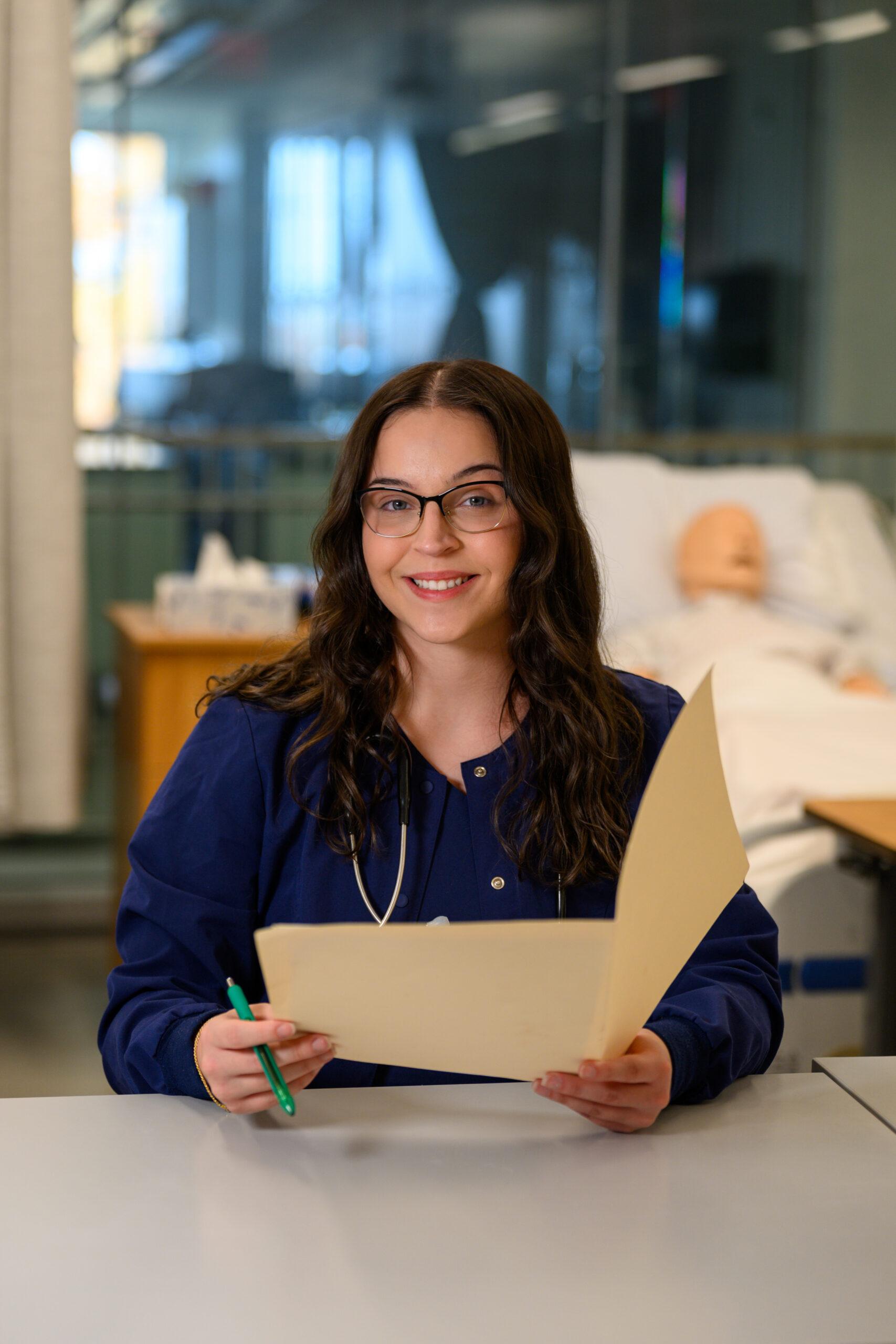 Female student smiling at the camera while holding a folder